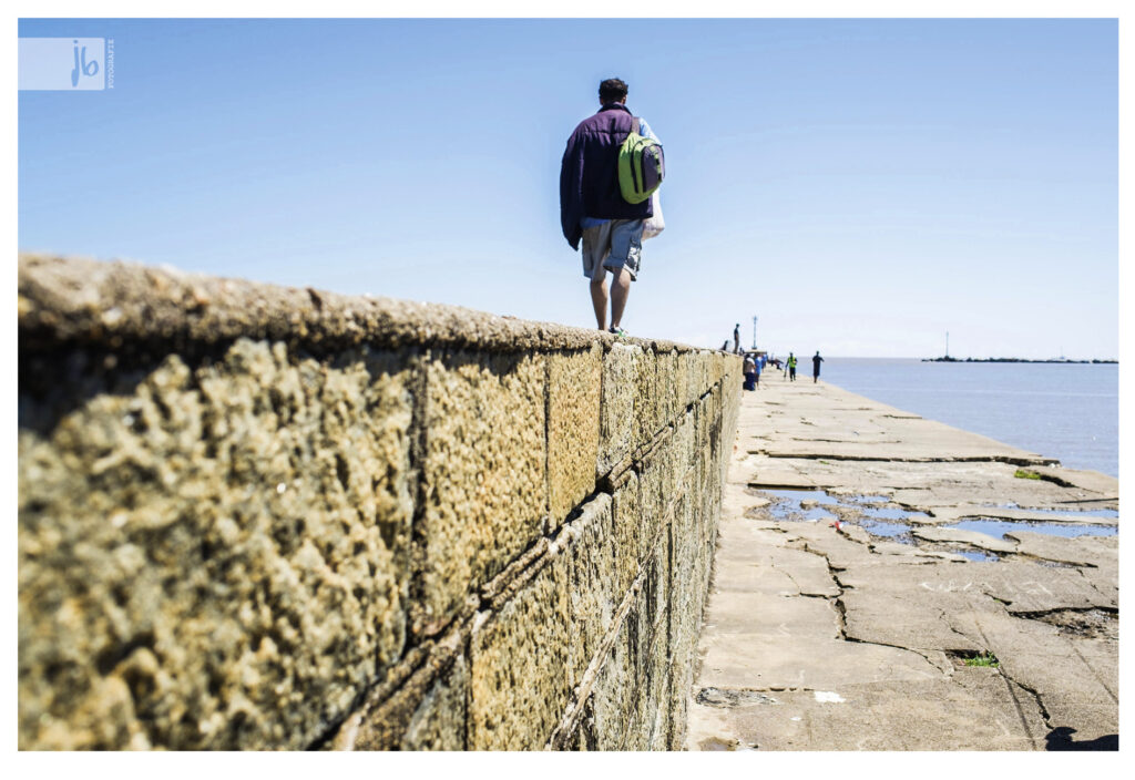 ein Mann läuft auf einer Mauer in Montevideo, rechts davon das Meer 