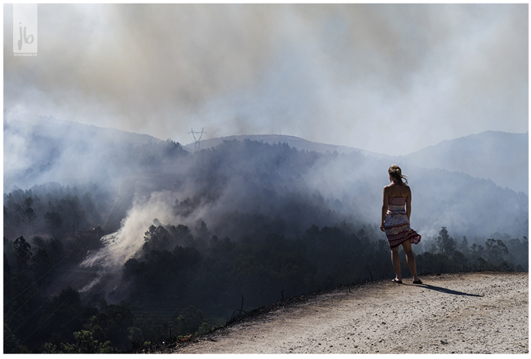 Waldbrand in Portugal und eine Frau steht im rot-weißen Kleid und blickt auf die Rauchschwaden