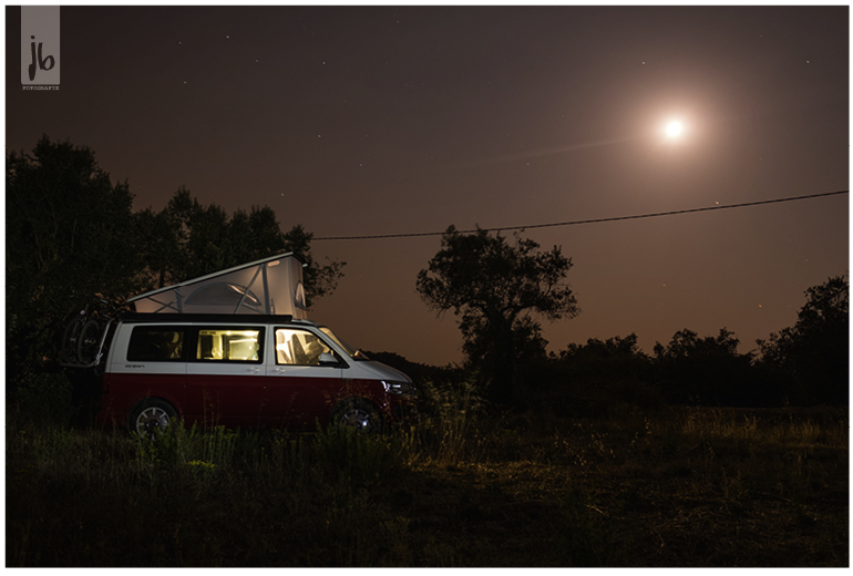 der VW Bus California Ocean in rotweiß auf seiner Wildcampingstelle in Portugal bei Nacht mit Beleuchtung von innen