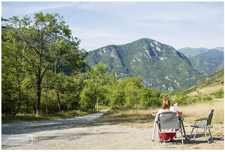 auf einem Parkplatz mit toller Aussicht auf einen Berg sitzt eine Frau auf Campingstühlen und frühstückt