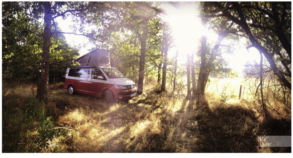 VW Bus California Ocean mit aufgestelltem Dach und der aufgehenden Sonne im Hintergrund an einer Wildcampingstelle