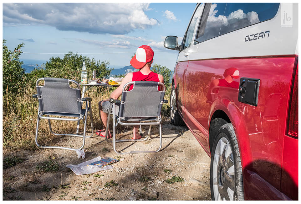 Camping mit dem rot weißen VW Bus California Ocean und seiner Campingausstattung die ein Mann nutzt der eine rot weiße Kappe trägt