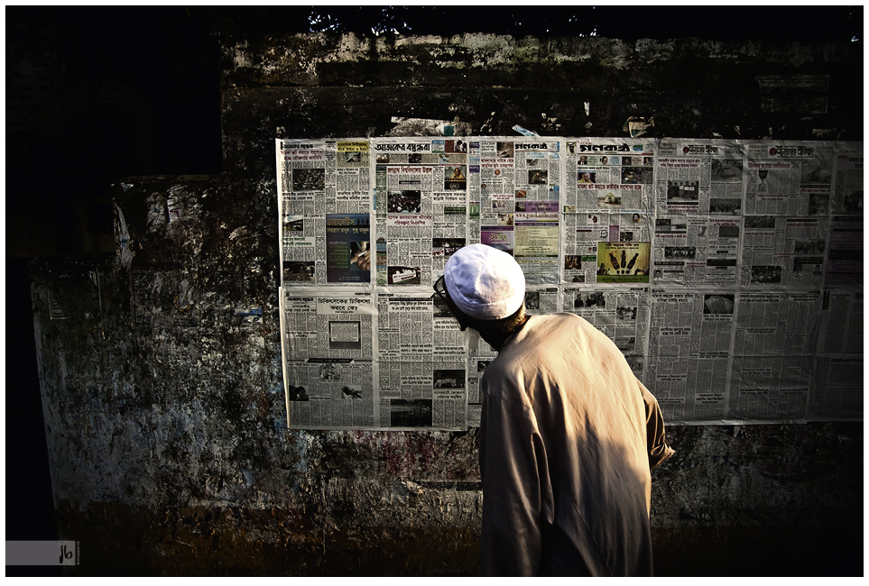 ein alter Bangladesch liest eine Zeitung, die öffentlich zugänglich an eine Mauer geklebt wurde