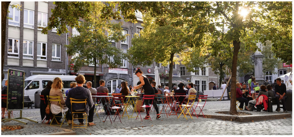 ein Café in Antwerpen mit bunten Stühlen und einem großen Baum durch den die Sonne scheint