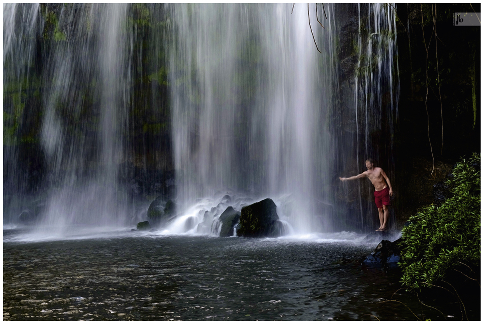 Langzeitbelichtung von einem Wasserfall bei dem ein Mann die Hand ausstreckt