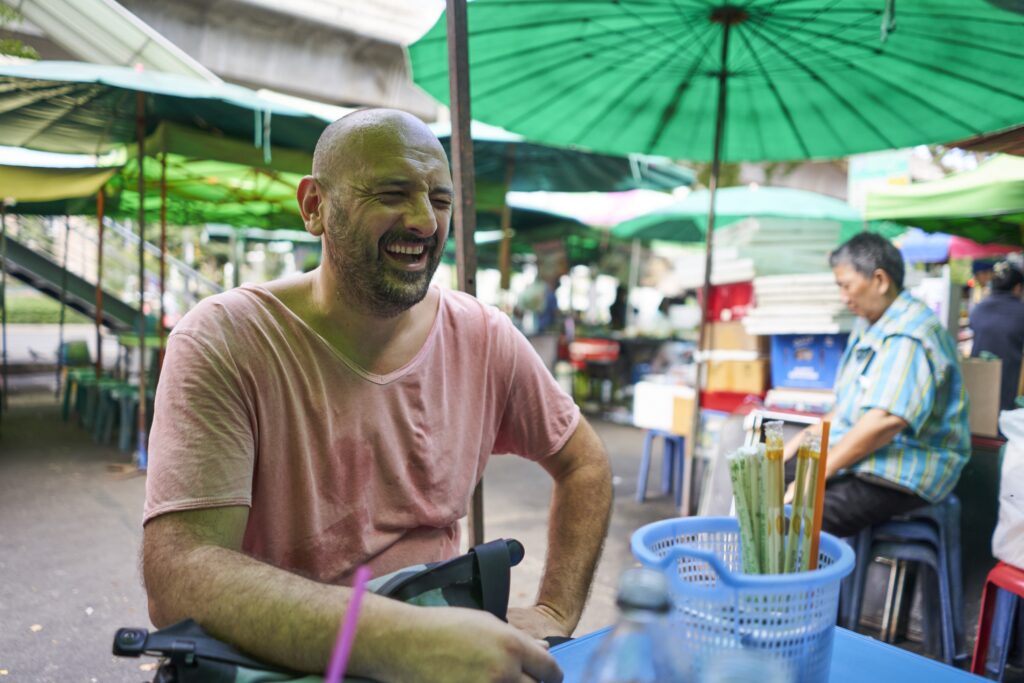 Ein Mann (Robert) lacht während wir in einem Streetfoodlokal in Bangkok auf unser Essen warten