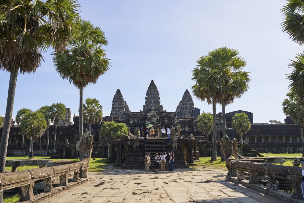 der Tempel von Angkor Wat umringt von Palmen. Auf einer Treppe gelangen die Touristen in das Weltkulturerbe