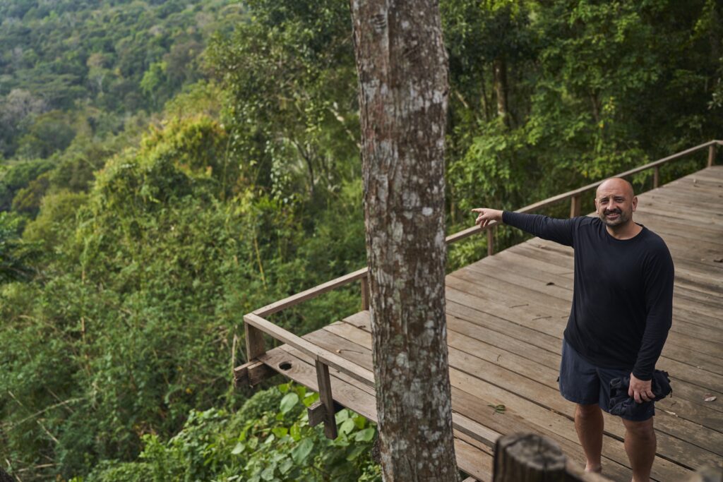 Ein Mann (Robert) zeigt von einer Aussichtsplattform in der Unterkunft des Mondulkiri Projects in Senmonorom auf den Urwald und sein dichtes Blätterdach