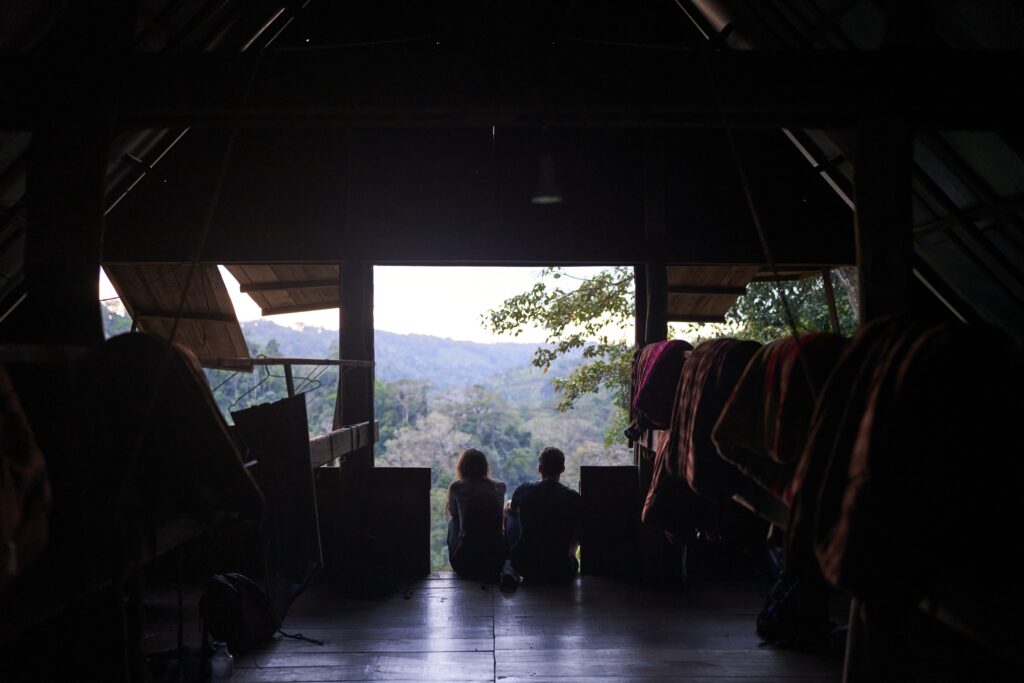 ein Paar sitzt im Schlafsaal und genießt die Aussichtsplattform in der Unterkunft des Mondulkiri Projects in Senmonorom auf den Urwald und sein dichtes Blätterdach