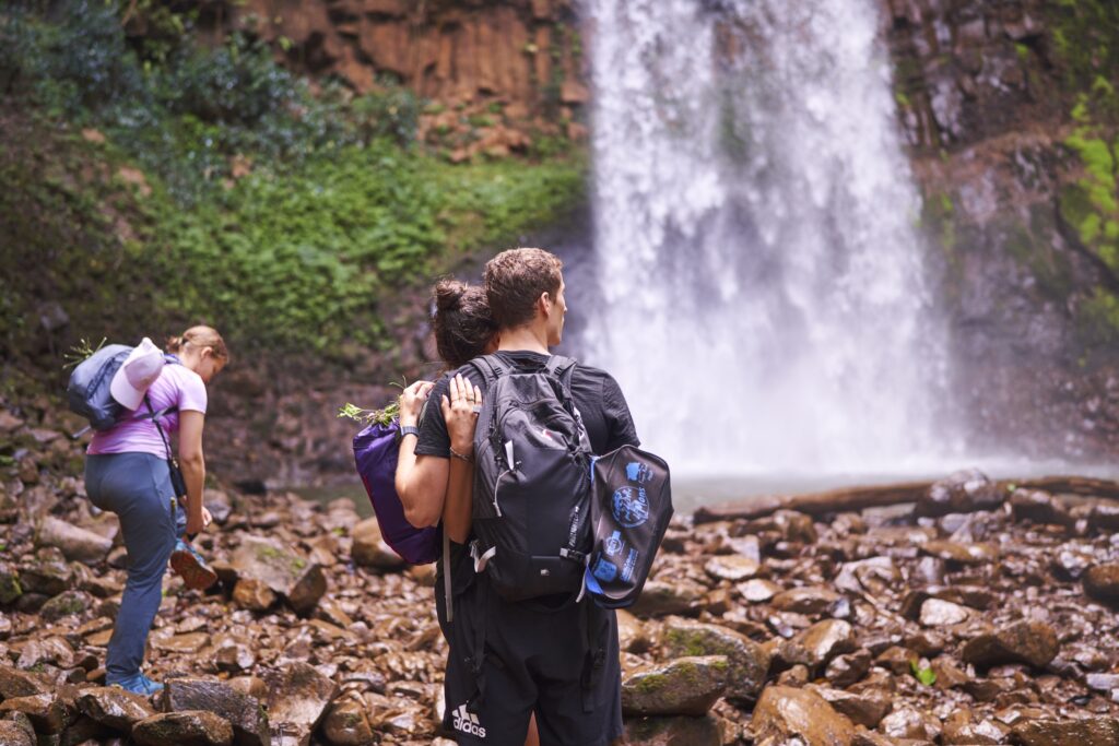 ein Paar mit Bambusringen steht Arm in Arm vor einem Wasserfall