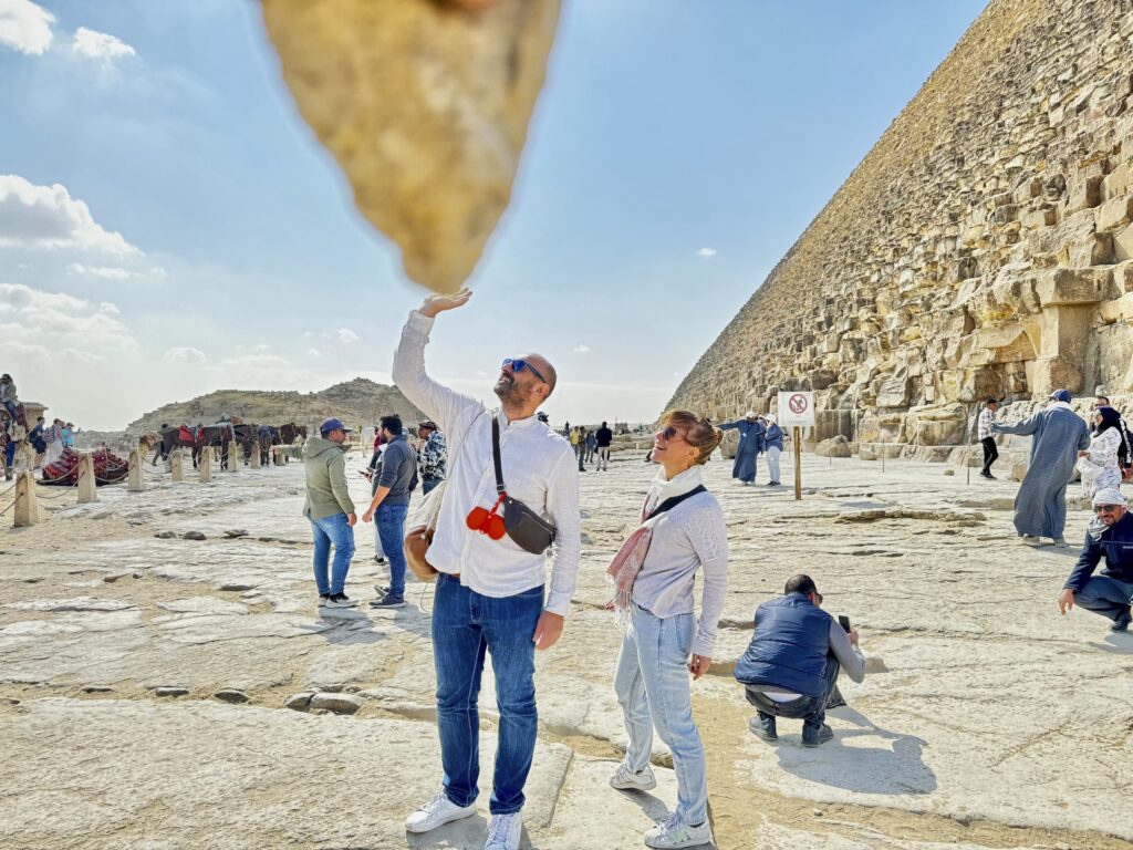 typisches Touribild an den Pyramiden; der Fotograf hält einen kleinen Stein ins Bild, während Robert so tun soll als würde er ihn mit einer Hand heben und ich überrascht tun muss.