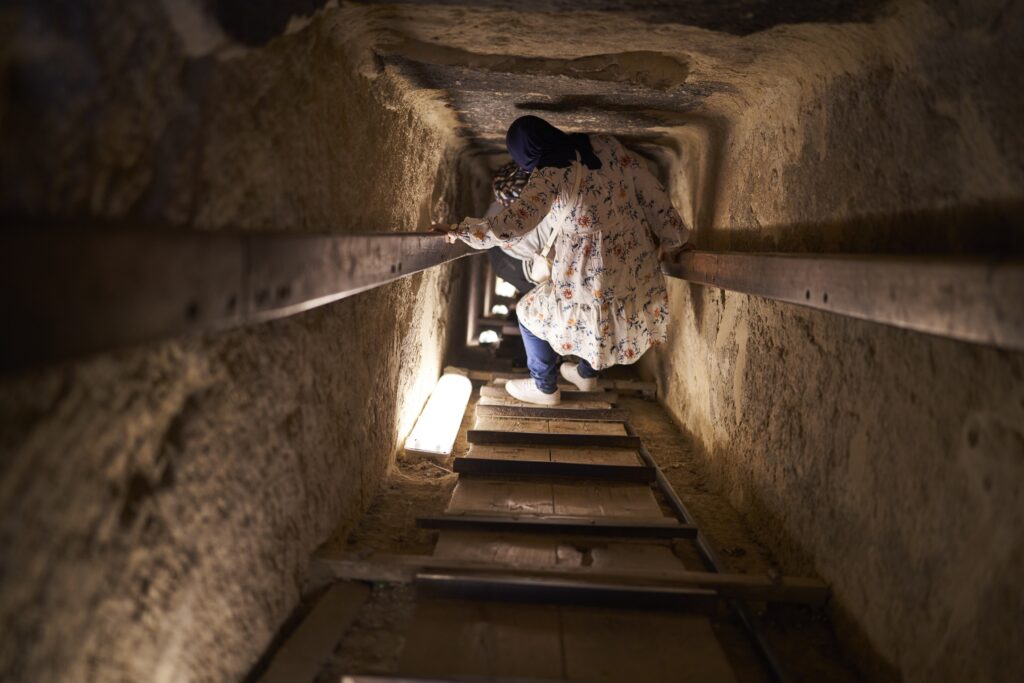 der Weg hinab in eine Pyramide ist steil und einzig eine Holzplange mit Streben gibt Halt