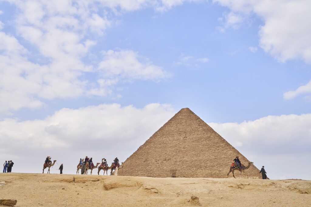 eine Pyramide und viele Kamele in einer Karawane davor