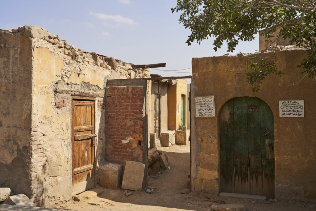 eine malerische Ecke in der Stadt der Toten in Kairo mit einer Holztür, einer Backsteinwand, einer grünen runden Tür und einem Bäumchen