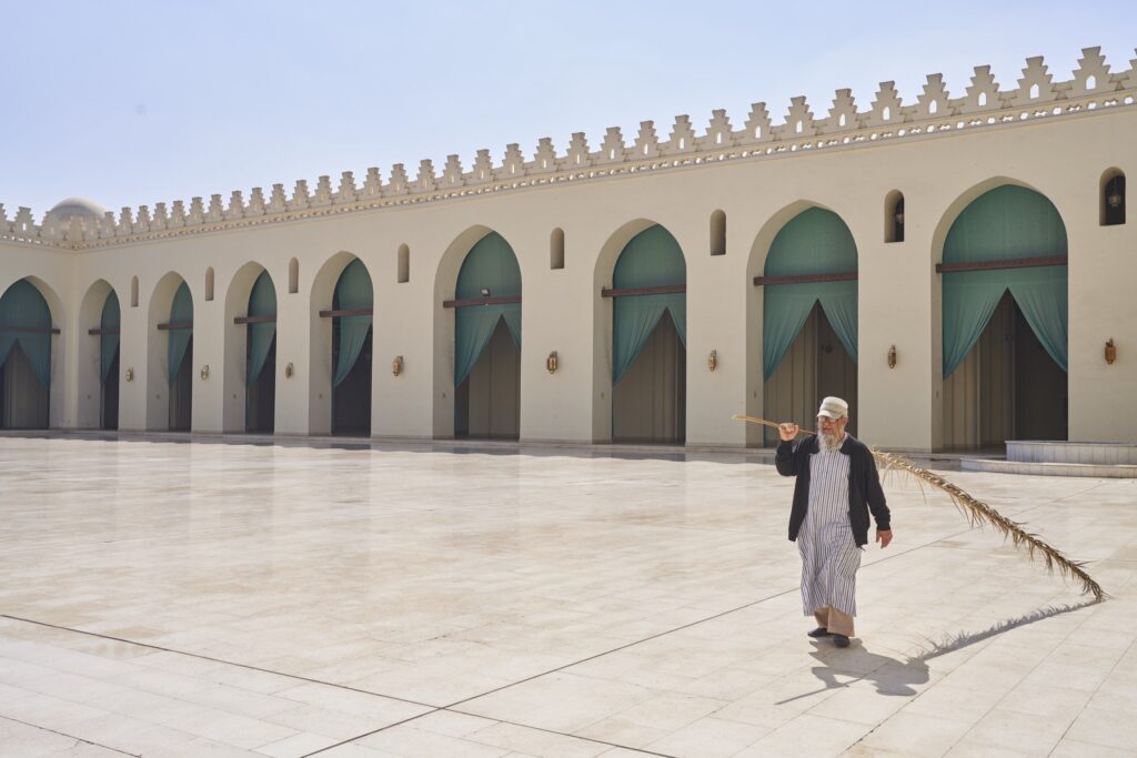 ein Mann mit einem Palmwedel geht über den großen Platz der weißen Moschee in Kairo.