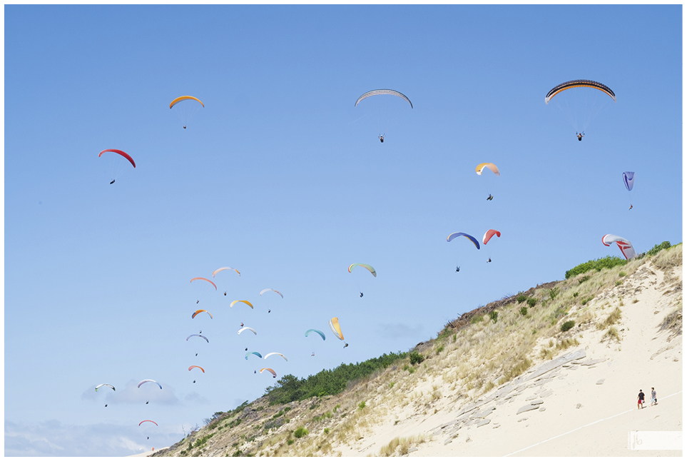 Paraglider an der Dune du Pilat tummeln sich mit bunten Schirmen in der Luft über der Sanddüne