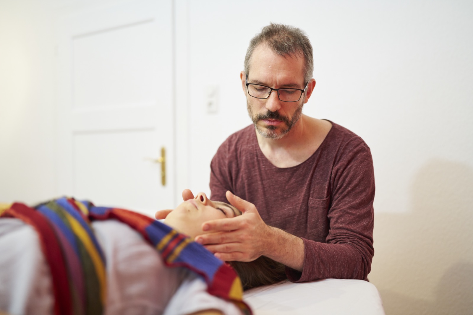 ein Heilpraktiker behandelt seine Patientin indem er ihren Kopf in Händen hält