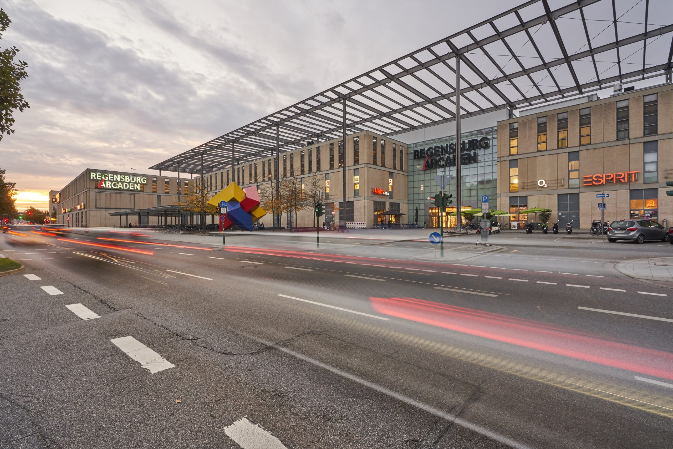 Die Regensburger Arcaden von außen mit Langzeitbelichtung und dadurch lange Lichtstreifen der vorbeifahrenden Autos.