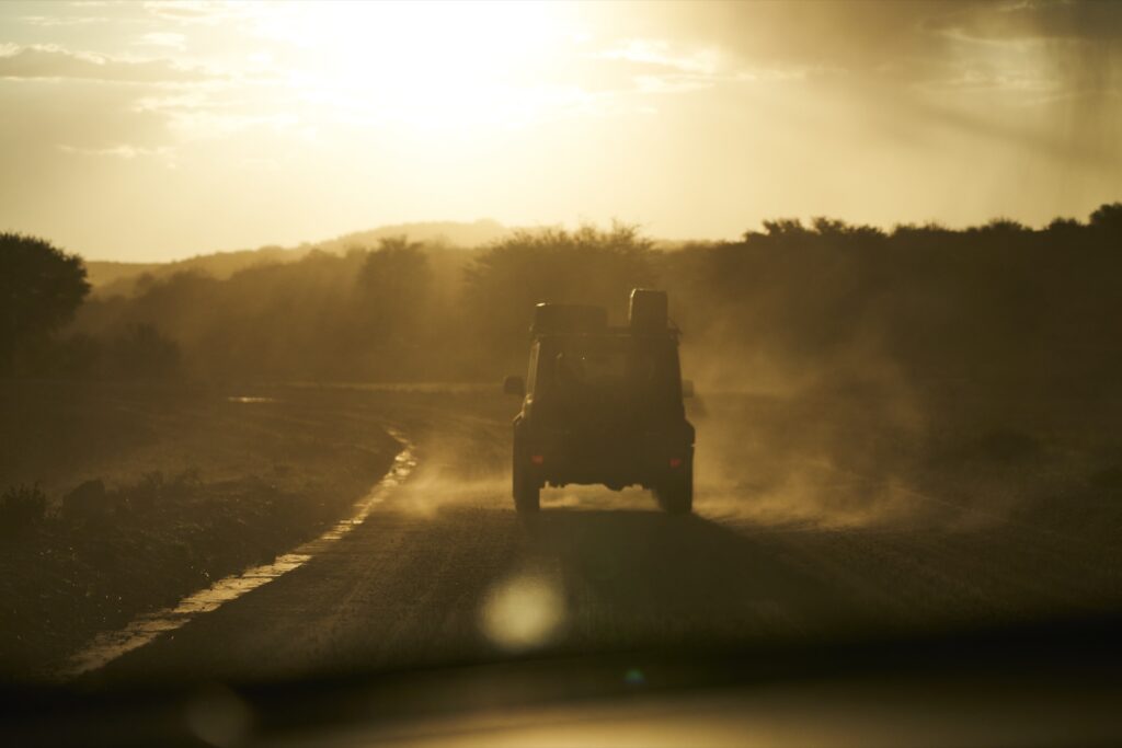 der Jeep vor uns wirbelt viel Sand auf im Gegenlicht im Kgalagadi Transfrontier National Park in der Kalahari in Südafrika